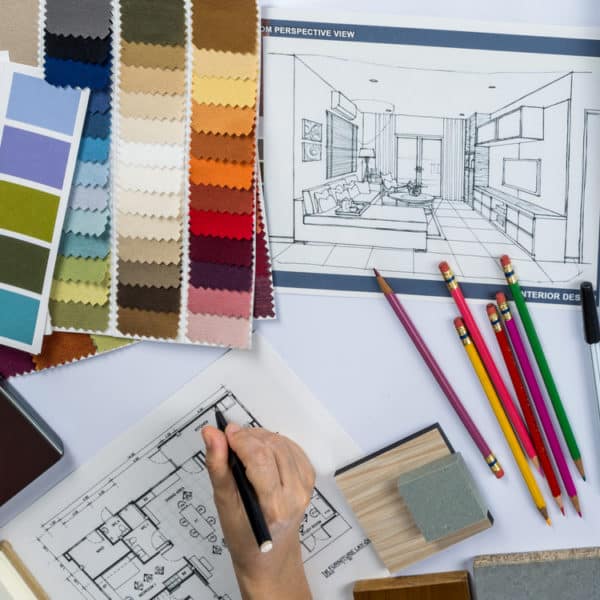An interior designer at work, creating a floor plan with fabric samples, colouring pencils and a perspective drawing scattered around the desk