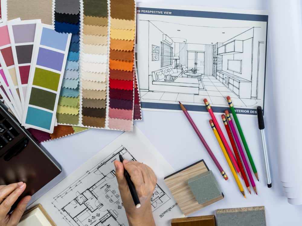 An interior designer at work, creating a floor plan with fabric samples, colouring pencils and a perspective drawing scattered around the desk
