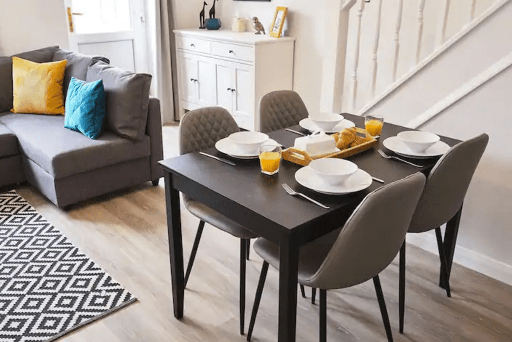 Small dining table with grey chairs in an open plan living space, with breakfast set up on the table