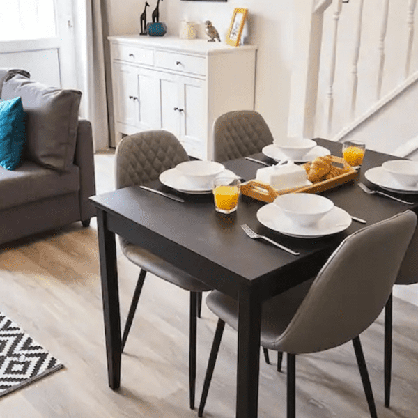 Small dining table with grey chairs in an open plan living space, with breakfast set up on the table