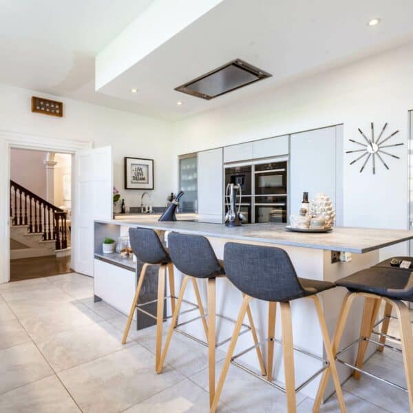 White modern slab kitchen with a breakfast bar kitchen island and five stools with grey upholstery