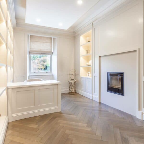 Spacious white home office with in-built shelving, a white desk and wooden parquet flooring
