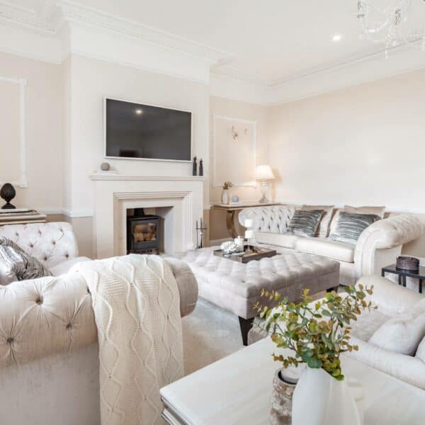 A classic living room in neutral colours, with two cream Chesterfield sofas and a Chesterfield pouffe footstool