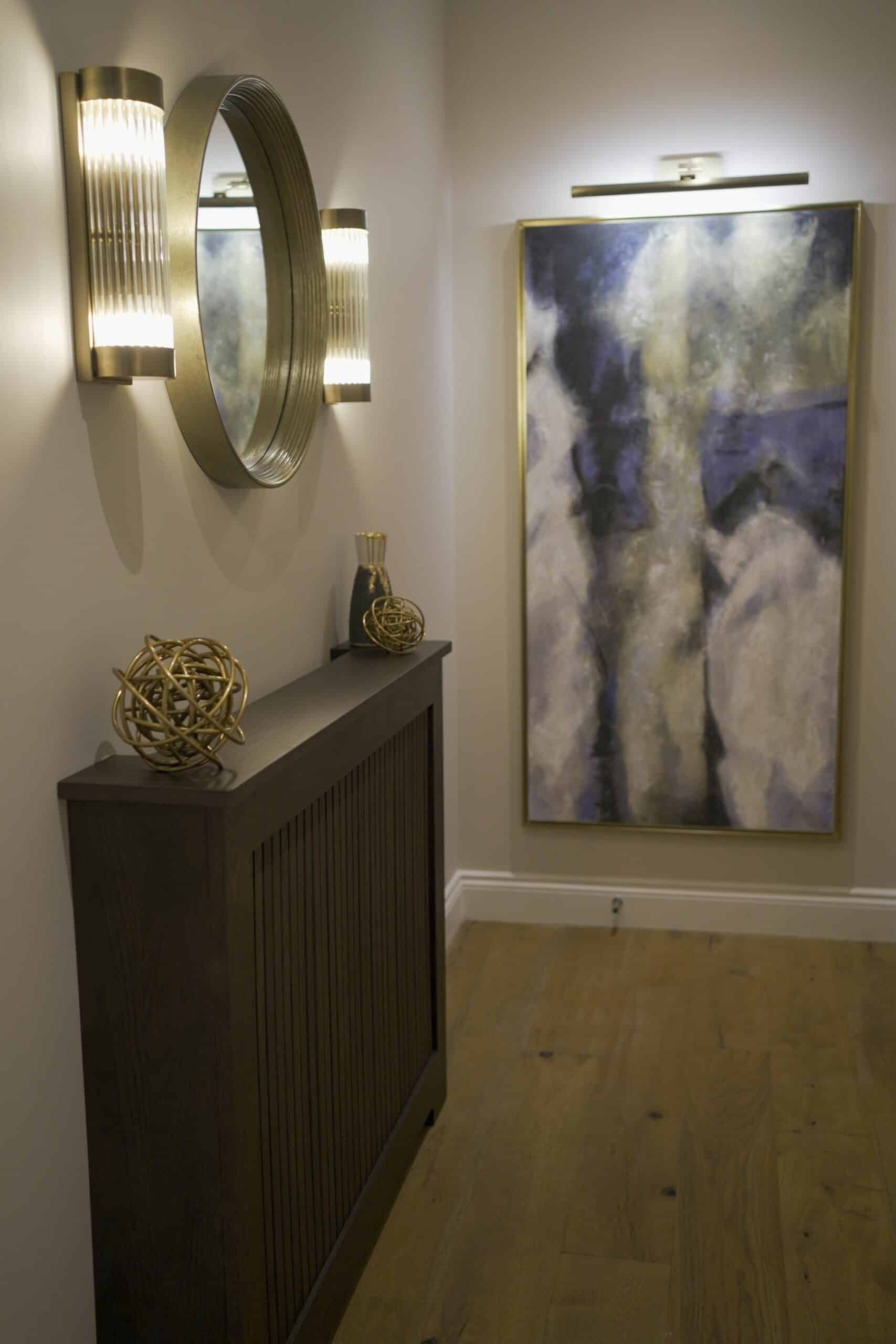 Neutral-coloured hallway with bespoke radiator cover, rounded mirror, tubular wall lights and modern art on the walls