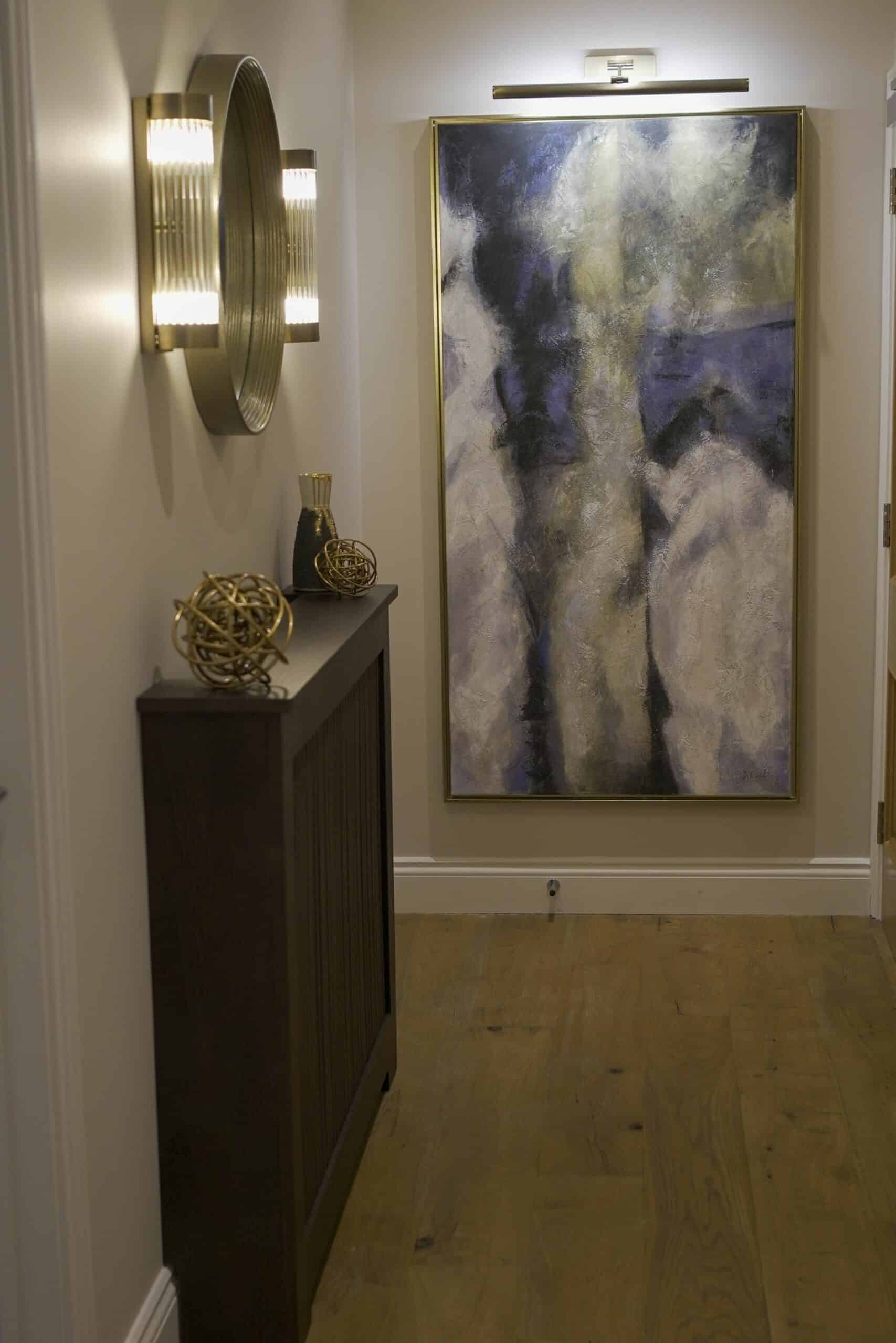 Neutral-coloured hallway with bespoke radiator cover, rounded mirror, tubular wall lights and modern art on the walls