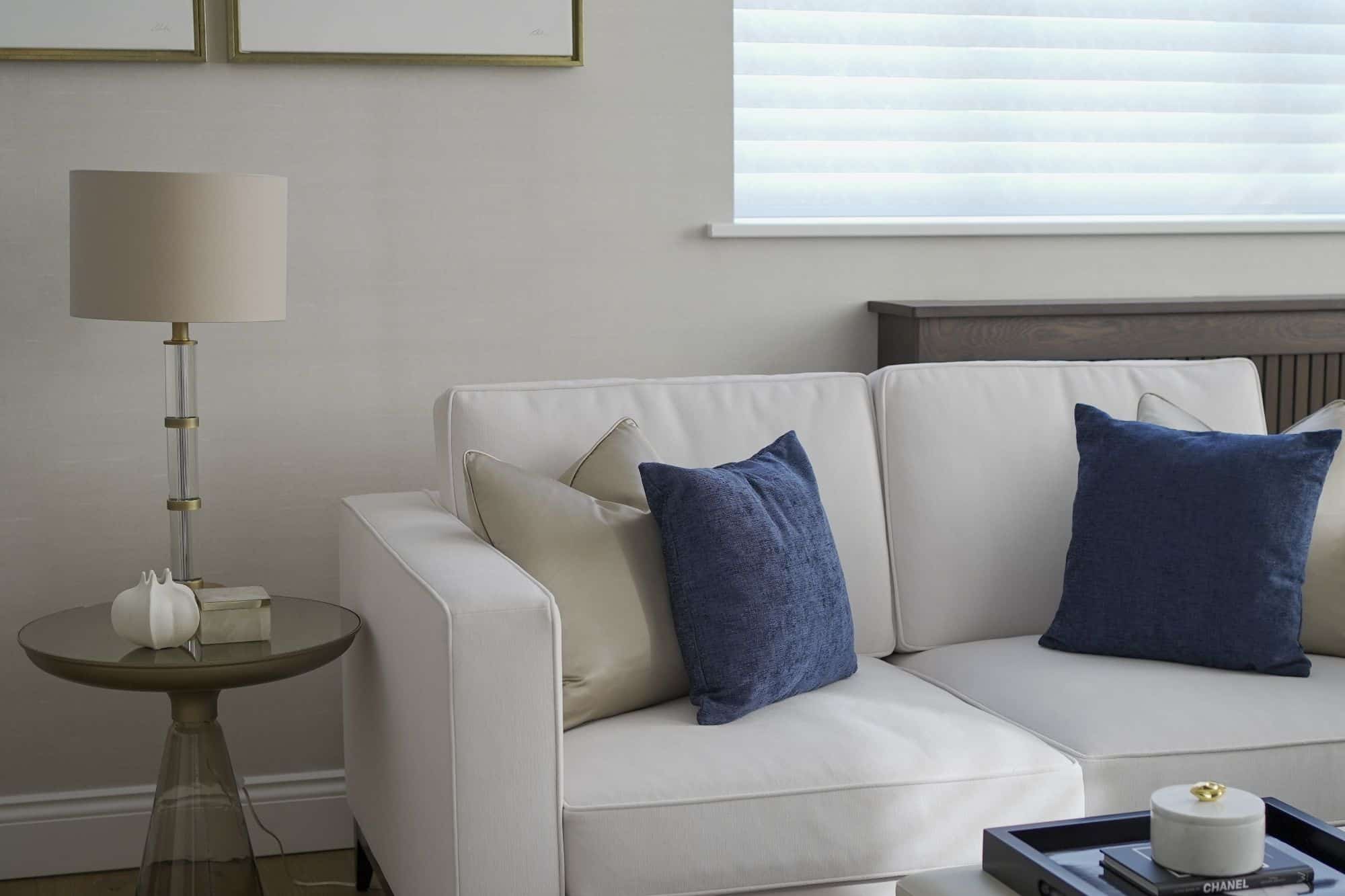 A modern sitting room in muted colours with a modern sofa and glass-based side table